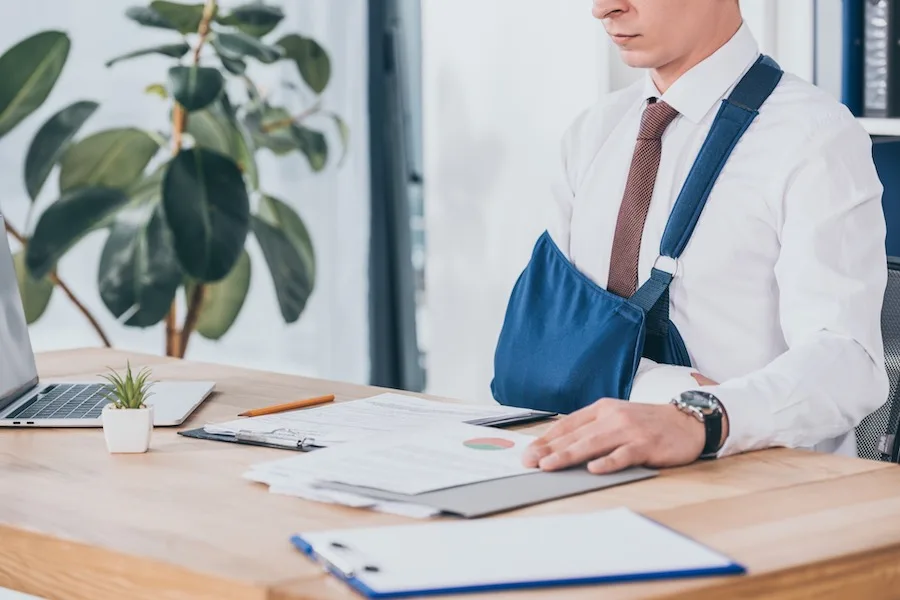 Person With A Broken Hand Looking At Documents Set On A Table